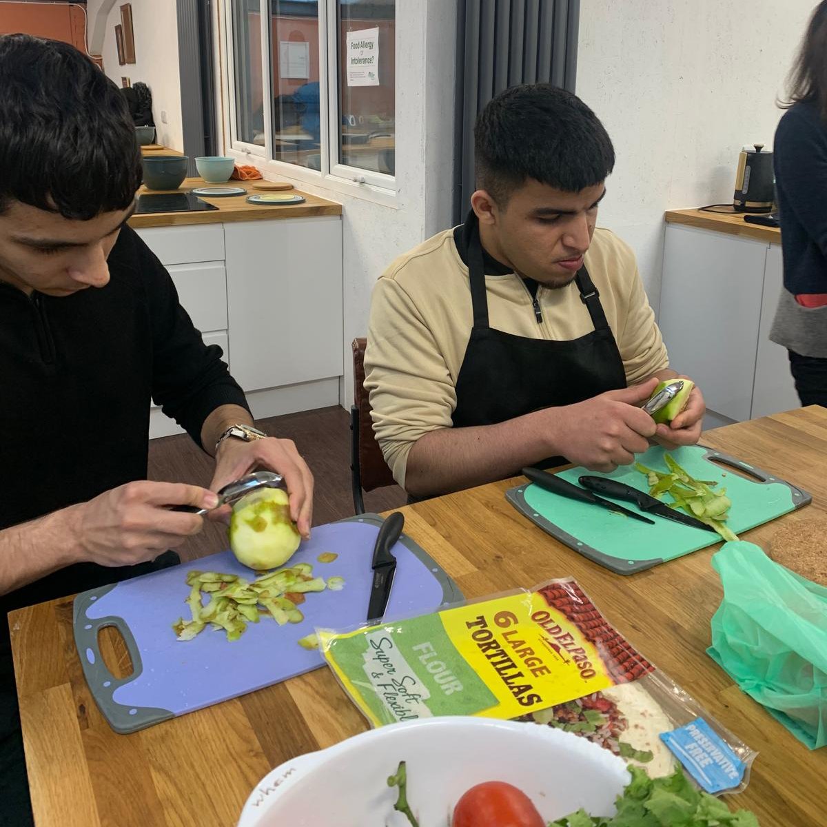 Two young men preparing fresh vegetables on chopping boards