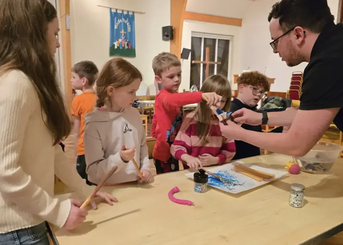 Group of children doing craft activities at a table being guided by an adult