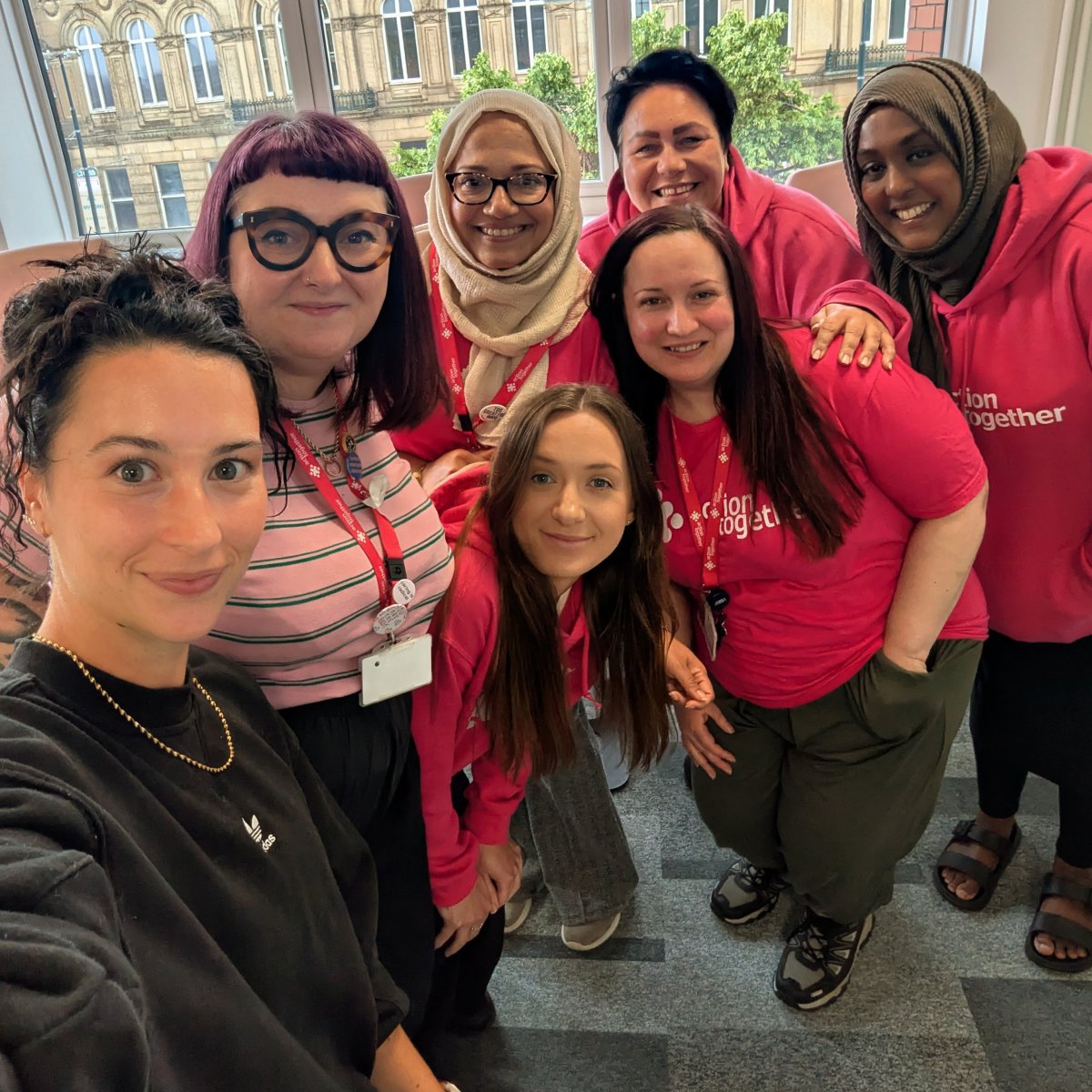 Group shot of all Volunteer Team members smiling and wearing pink hoodies