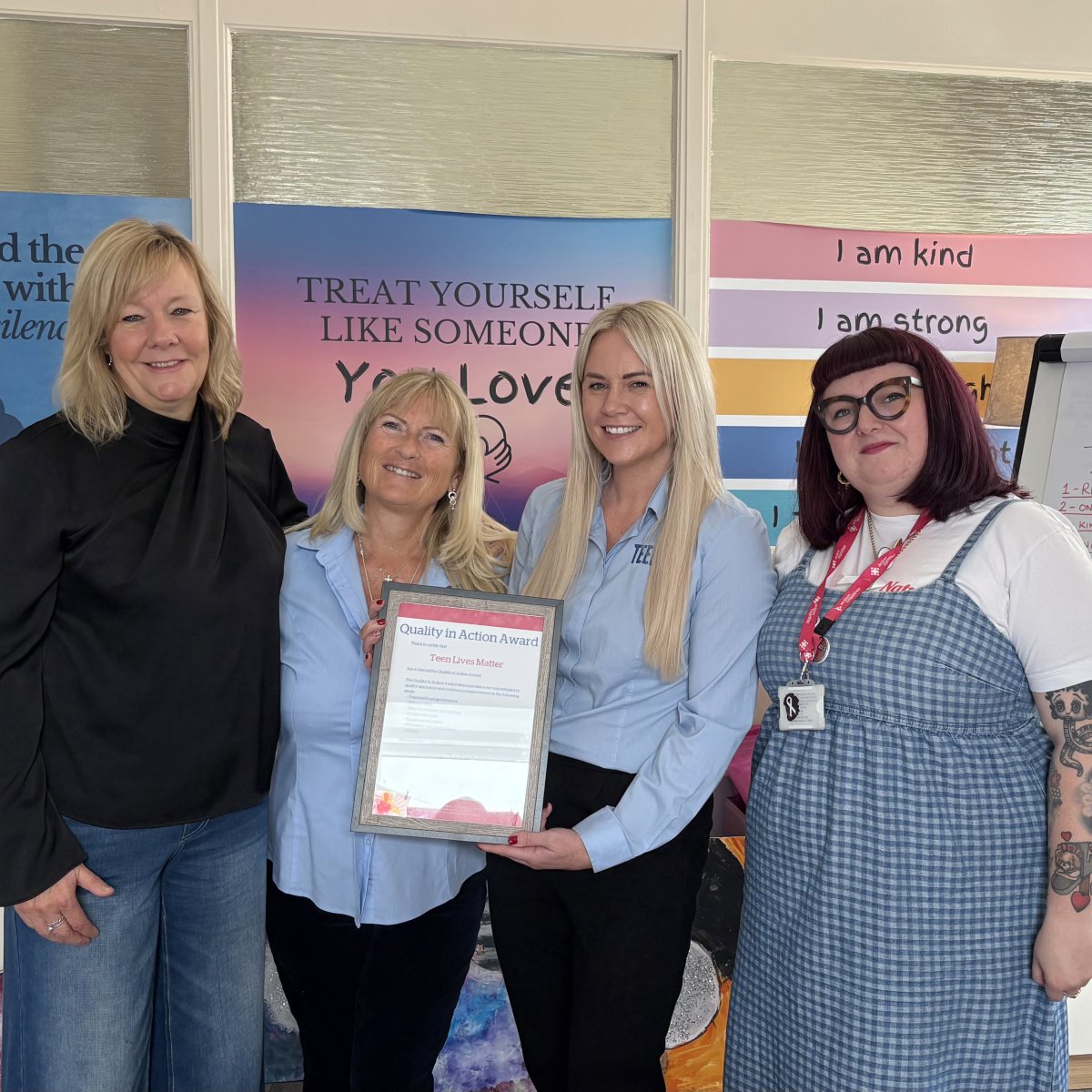 Four smiling women - two Teen Lives Matter colleagues receiving QiAA certificate from two Action Together employees 