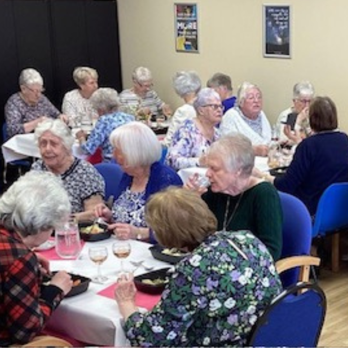 Room full of elderly people seated at tables enjoying cooked meals
