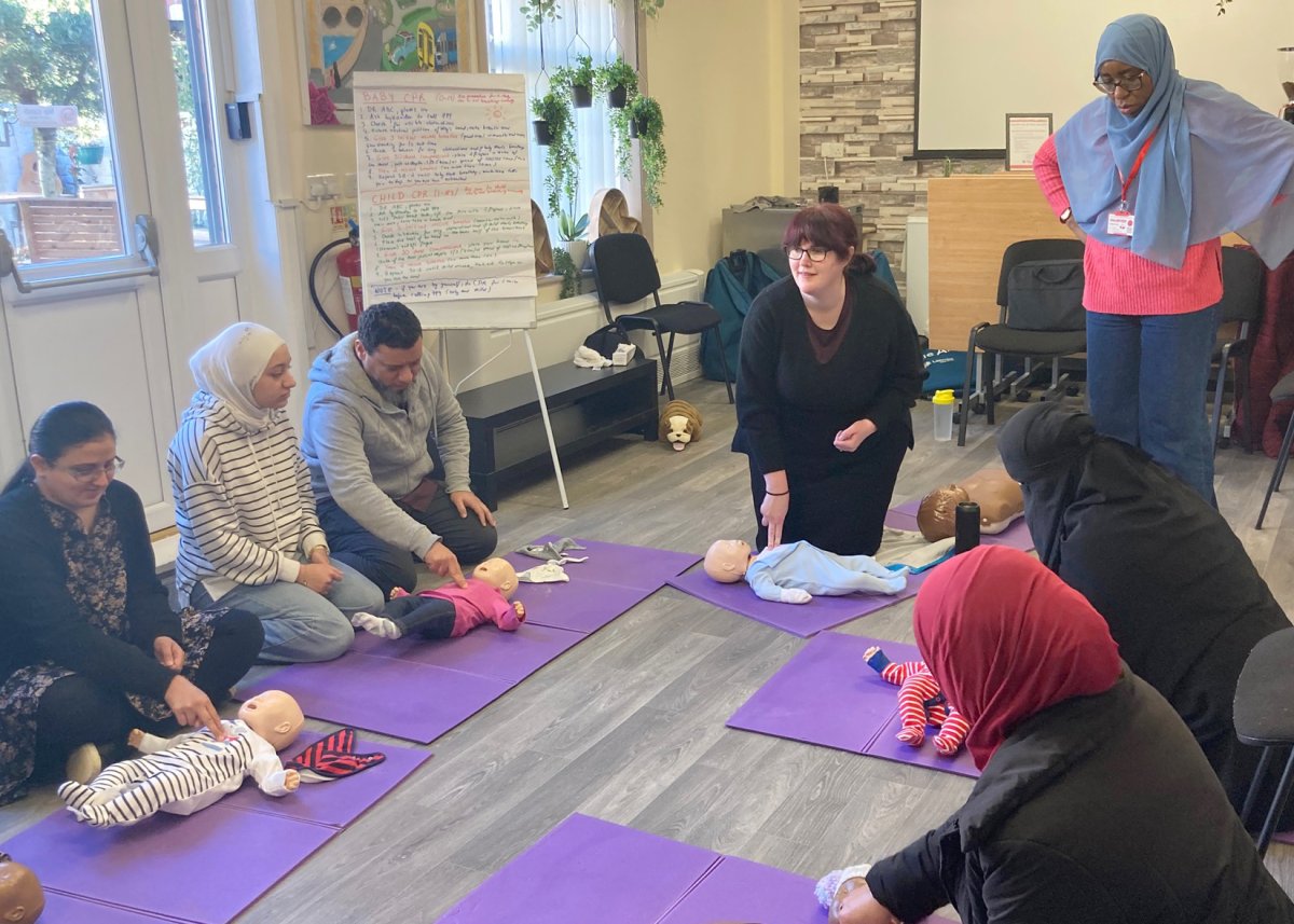 Group of people sat on floor with dummy babies, attending paediatric first aid training session with Kate from Kate's Training CIC