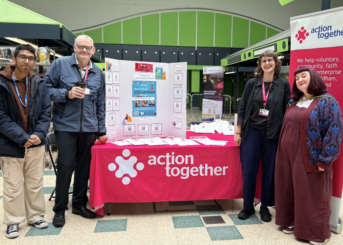 Action Together team members stood around Volunteer Fair stall smiling at camera