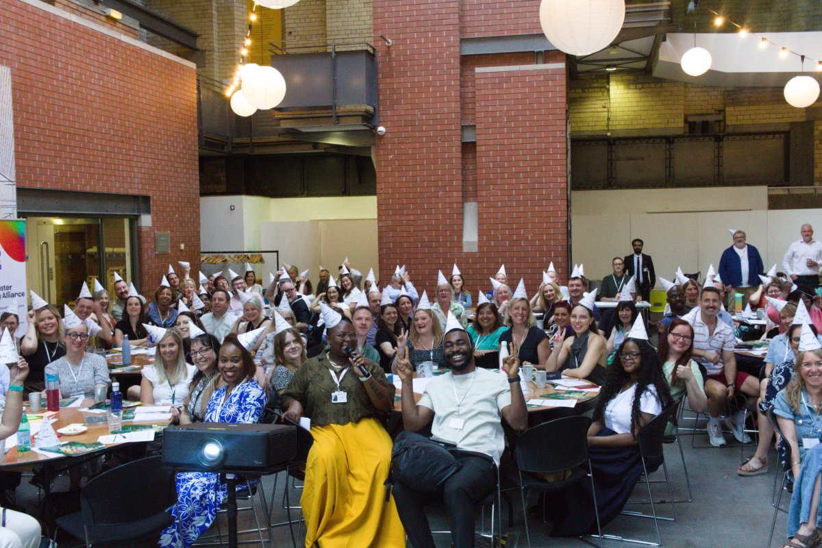 Room full of people seated around tables at event wearing white party hats