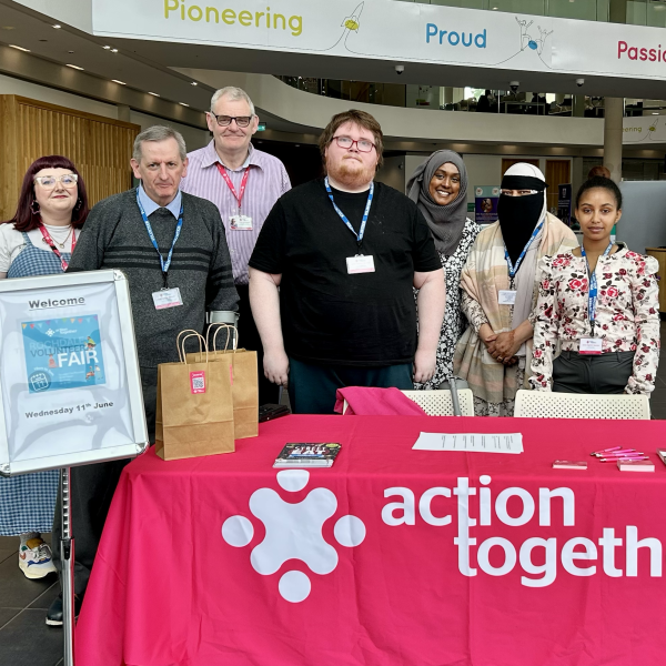 Rochdale Volunteer Team and volunteer helpers at the Volunteer stood behind Action Together stand with pink tablecloth and logo